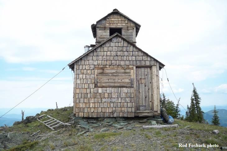 A wood-shingled lookout located on top of a mountain.